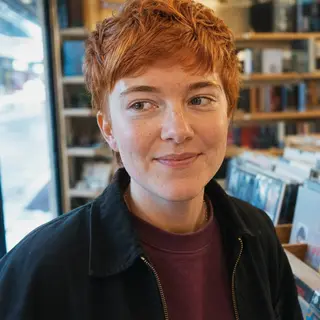 Natural customer-style portrait of a person wearing a dark jacket and plum sweatshirt in a record shop