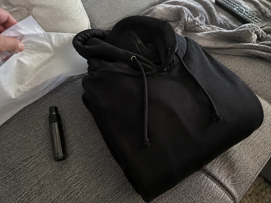 Candid sofa flat lay of a dark sweatshirt, scent atomisers and everyday accessories