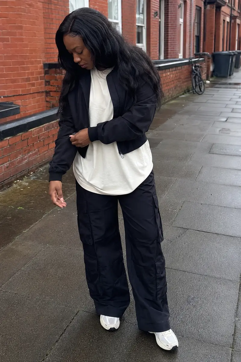 Phone-style street photo showing black cargo trousers, a cream T-shirt and black jacket