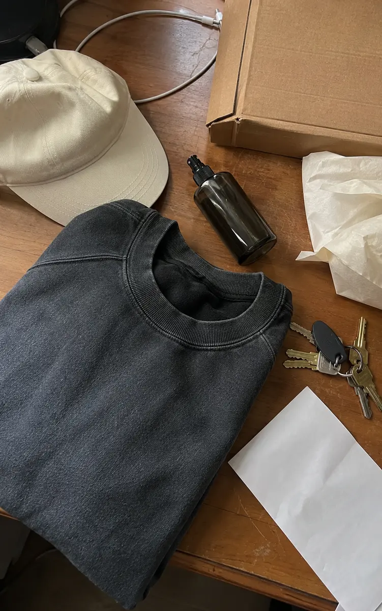 Phone-style top-down photo of a washed sweatshirt, cream cap, atomiser and parcel