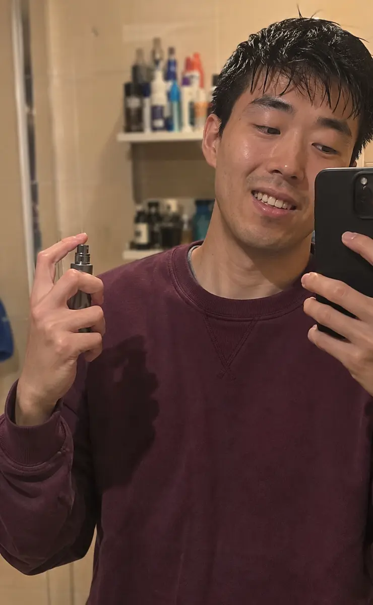 Phone-style bathroom mirror photo showing a plum sweatshirt and small atomiser