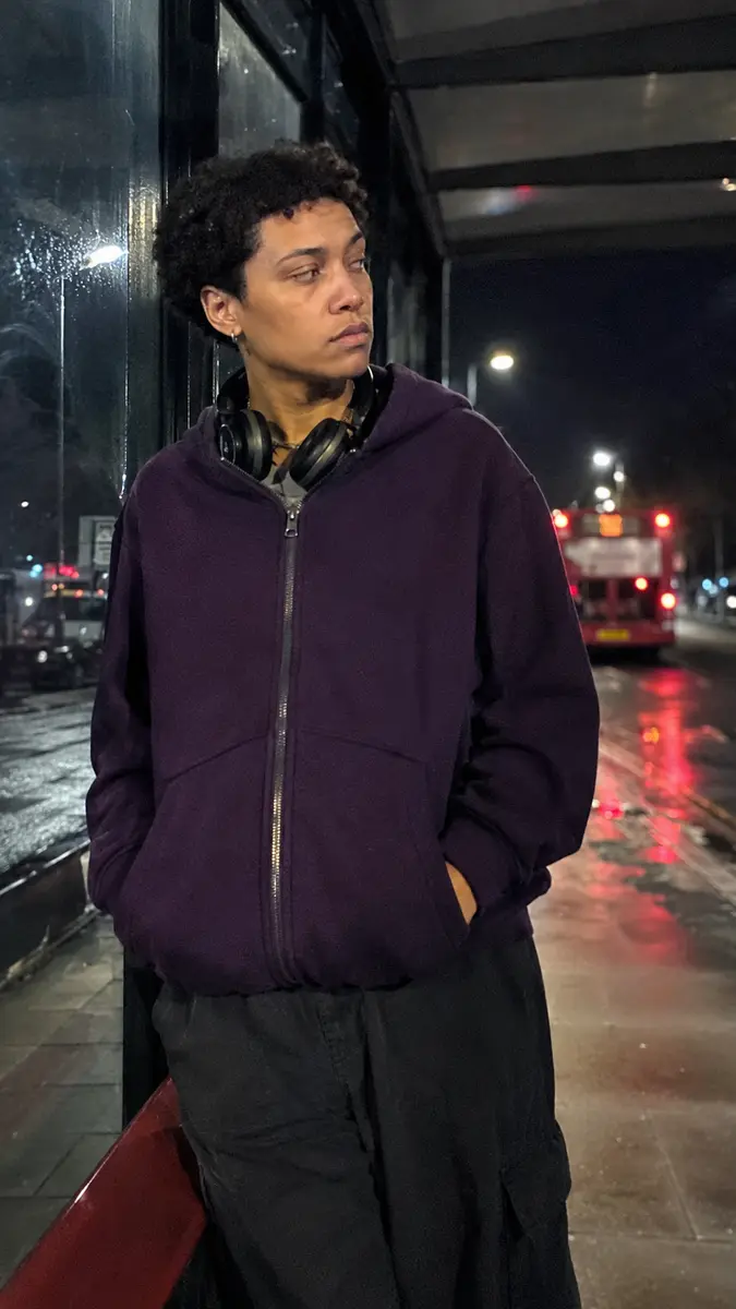 Phone-style night photo showing a dark-purple zip hoodie at a bus stop